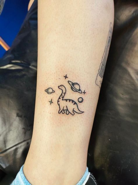 Small dinosaur tattoo in space. T Rex Space Tattoo, Patchwork Dinosaur Tattoo, Cute Tattoos Dinosaur, Cute Dino Tattoo Matching, Star And Space Tattoos, Cute Matching Dinosaur Tattoo, Dino Tattoos Cute, Cow On A Skateboard Tattoo, Dinosaur Tattoo Aesthetic