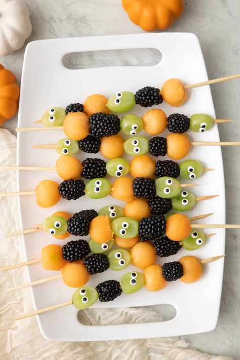 Get ready to spookify your taste buds with our Halloween Fruit Kabobs! These ghoulishly delightful skewers feature juicy cantaloupe balls that are like mini pumpkin orbs, grapes with mischievous googly eyes that seem to watch your every move, and plump, mysterious blackberries that add a dark twist to your fruit adventure. It's a fruity fiesta that's as playful as it is eerie – the perfect way to haunt your taste buds this Halloween! Grab one and take a bite, if you dare! | Halloween F Halloween Fruit Class Party, Fruit Kabobs Halloween, Pumpkin With Fruit Skewers, Halloween Fruit Skewers For Kids, Spooky Fruit Salad, Pumpkin Fruit Kabobs, Halloween Snacks Fruit, Fruit Halloween Tray, Halloween Fruit Kabobs For Kids