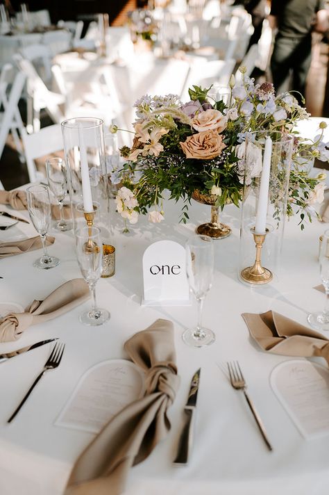 Gold Centerpiece Vase and White Taper Candles in Short Brass Candlesticks | Trendy Neutral Wedding Decor Ideas | Muted Pastel Florals Muted Neutrals Wedding, Boho Wedding Centerpieces With Candles, Oval Table Wedding Decor, Ivory Pillar Candles Wedding, Candle And Flower Centrepiece, Pastel Neutral Wedding, Wedding Flowers For Round Tables, Gold Candlestick Wedding Centerpieces, Wedding Ideas White And Gold