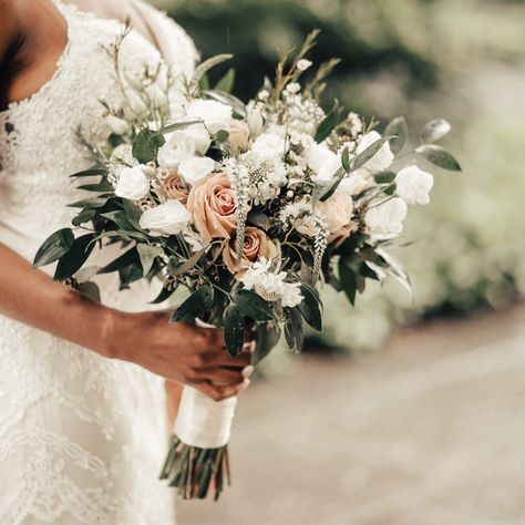 A lush bohemian style white and cream hand-tied bouquet designed with a selection of seasonal blooms such as Roses, Spray Roses, Wax Flower, Veronica and Lisianthus with lush accenting greenery. The stems are artfully wrapped with a double-satin Ivory ribbon for a luxurious finish.