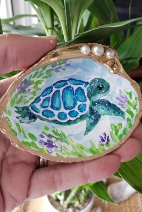 Photo shows a clam shell hand painted with a blue and green sea turtle.  The shell is edged in gold leaf and decorated with small pearls. Clam Shell Art Projects, Painted Clam Shells Ideas, Clam Shell Painting, Sea Shell Painting Ideas, Painting On Seashells, Clam Painting, Shell Painting Ideas, Sea Shell Painting, Dollar Art