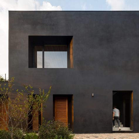 A matte-black rendering called Corev Mooth covers the walls of this residence, while window frames and shutters are made from a tropical tzalam wood coated in reddish sealer as a contrast.  Called Las Golondrinas, the house is composed of three volumes topped by a large sloped roof to create a covered patio that opens onto a swimming pool that aligns with the tree canopy. Matte Black House, Stone Deck, Basement Floor Plans, Stucco Homes, Weekend House, Black House Exterior, Good House, City House, Black Exterior