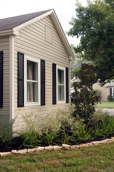 Fixer Upper hosts Chip and Joanna Gaines repainted the siding a neutral shade and the shutters black for a fresh updated to the exterior. They also updated the landscaping and added new grass. Exterior Door Colors With Tan Siding And Black Shutters, Black Front Door Tan House, Tan Ranch House Exterior, Tan And Black Exterior House, Tan Siding Black Shutters, Tan Siding House, Tan Exterior House, Tan And Black House Exterior, Tan House Exterior Color Schemes