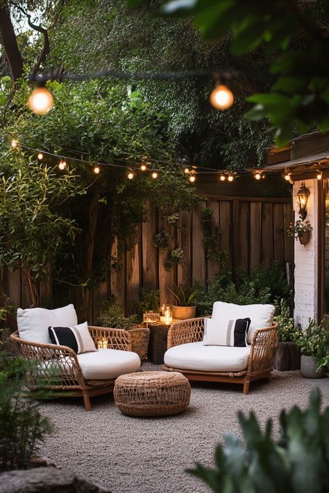 Cozy outdoor lounge area with string lights, two wicker chairs with cushions, and a round ottoman, surrounded by lush greenery. Small Patio Sitting Area Ideas, Small Backyard Decorating Ideas On A Budget, Backyard Patio Ideas On A Budget Outdoor Areas Pea Gravel, Small Backyard Ideas Apartments, Builder Grade Patio Makeover, Easy Cheap Backyard Ideas, Rental Friendly Backyard Ideas, Small Patio Landscaping Ideas, Cozy Patio Ideas On A Budget