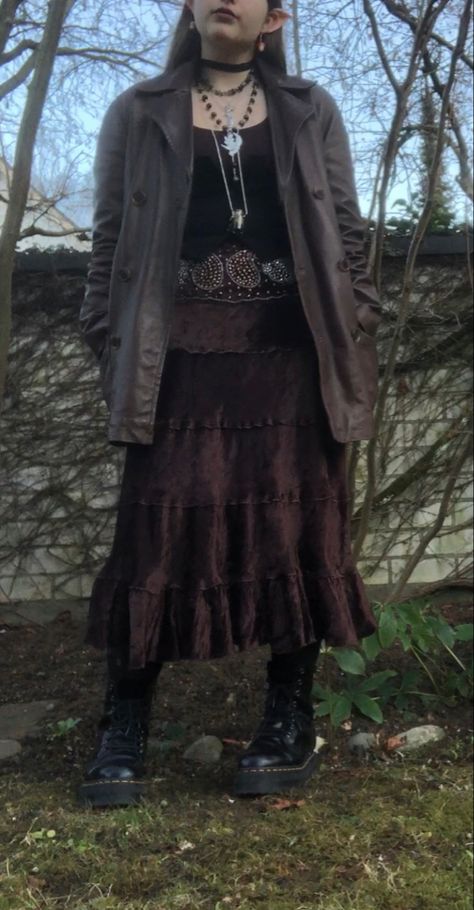 A mid-size person/girl wearing mate rose lipstik, a black tight waistcoat with a ripped stocking selfmade longsleeve and a thrifted dark brown maxi skirt, black dr. Martins and multiple crystal rings and bracelets. 	The person is also wearing multiple silver necklaces, one in form of a dragonfly and another in form of a moon, a green crystal bead necklace and a black lace choker. Dark Witchy Outfits Aesthetic, Dark Forest Core Outfit, Dark Fairycore Costume, Woodland Goth Aesthetic Outfits, Autumn Fairycore Outfits, Cottage Goth Aesthetic Outfits, Cottage Punk Fashion, Cottage Core Goth Outfits, Fairy Core Winter Outfits