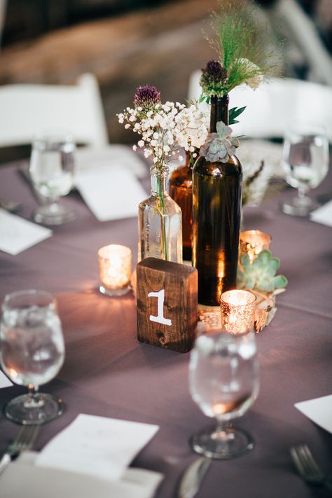 vintage wine bottle centerpiece idea Wedding Centerpieces Bottles, Bourbon Bottle Wedding Centerpieces, Wine Bottle Vases Centerpiece, Wine Bottle Table Decor, Bourbon Bottle Centerpiece, Whiskey Bottle Centerpiece, Wine Bottle Wedding Decor, Wine Bottle Table Numbers, Wine Bottle Centerpiece