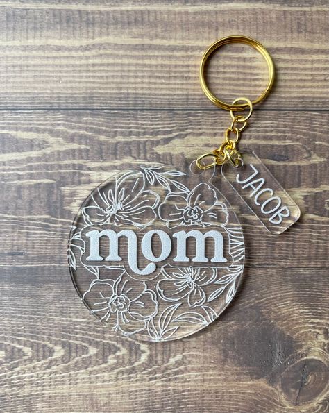 "The perfect small gift for that mom on Mother's Day! Made with clear acrylic, engraved and cut on Glowforge. Measures approx 2.75\" round and 1/8\" thick. Add your little ones name(s) on attached charm. Comes with gold keychain hardware." Vinyl Craft Ideas To Sell, Laser Engraved Acrylic Keychain, Acrylic Engraved Keychain, Acrylic Engraving Ideas Cricut, Mothers Day Acrylic Keychain, Acrylic Key Chains Designs, Clear Acrylic Laser Projects, Cricut Key Chains Vinyl, Cricut Projects Engraving