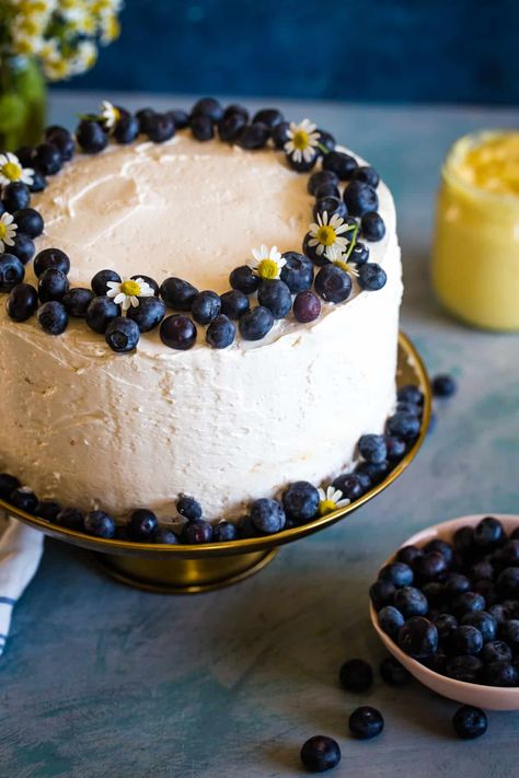 blueberry lemon curd cake on gold cake stand with bowl of blueberries in front and jar of curd in back. Light Birthday Cake, Lemon And Blueberry Cake, Lemon Blueberry Birthday Cake, Blueberry Lemon Curd Cake, Blueberry Lemon Custard Cake, Lemon Cake Decoration, Lemon Blueberry Cake Decoration, Birthday Cake Blueberry Decoration, Lemon Blueberry Cake