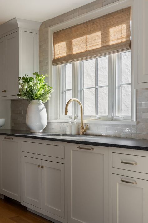 Kitchen with natural straw window shade Roman Shades On Black Windows, Kitchen Sink Roman Shade, Kitchen Window With Backsplash, Kitchen Sink Picture Window, Roman Shades In Kitchen Window, Triple Window Over Kitchen Sink, Large Window Kitchen Sink, Window Kitchen Backsplash, Picture Window Above Kitchen Sink