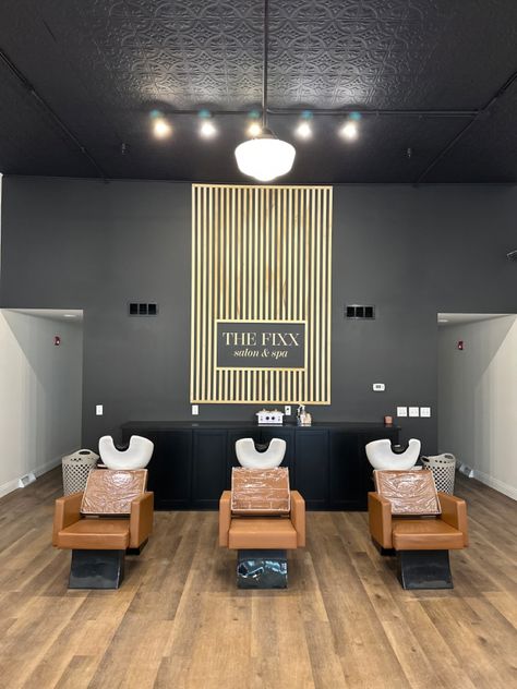 Black wall with vertical poplar wood slats, creating an accent wall. In the center, it says “THE FIXX SALON & SPA” Accent Wall For Salon Suite, Hair Salon Feature Wall, Salon Suite Accent Wall Ideas, Salon With Black Walls, Black Accent Wall Salon, Salon Picture Wall Ideas, Black And Wood Salon Decor, Black Wall Salon, Hair Salon Accent Wall