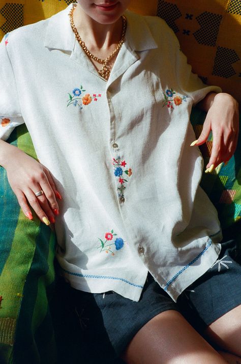 Short sleeve antique linen shirt in soft white with Madeira embroidery of little flower bouquets in blue, orange, and green. Boxy fit and camp collar. 4 mother of pearl button closure. Features special light x dark blue embroidered trim above and around the bottom hem. The majority of Behen's pieces are made either with very delicate fabrics and techniques or with antique textiles. All wear, mending, and idiosyncrasies are unique to the original fabric and are considered signs of love. Measurements (laying flat): Size Medium: Bust 43, Waist 43, Length 29, Shoulder 17.5, Sleeve 83/4 Michael is 5'9 with a 28" waist, and wears size medium with the Rock Jeans in Nonna. Laurence is 5'8 with a 27" waist, and wears size medium with the Linen Shorts in Soller and Vigna Necklace. Material: 100% lin Flower Embroidery On Shirt, Shirt Flower Embroidery, Embroidered Linen Top, Floral Embroidery Shirt, Embroidered Shirt Collar, Embroidery White Shirt, Button Up Embroidery, Embroidered White Shirt, Embroidery Shirt Ideas