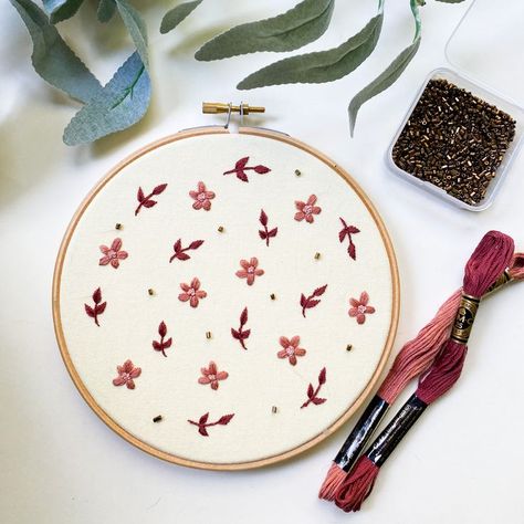 An image of a 6" embroidery hoop on a white background surrounded by props including green leaves, a small container of gold beads, and two skeins of embroidery floss in pink and burgundy. The hoop has pale yellow fabric and a pattern of small flowers and leaves, embellished with small gold beads. Hoop Embroidery, Basic Embroidery Stitches, Small Beads, Wooden Hoop, Art Wall Art, Wall Art Wall, Yellow Background, Art Wall Decor, Pale Yellow