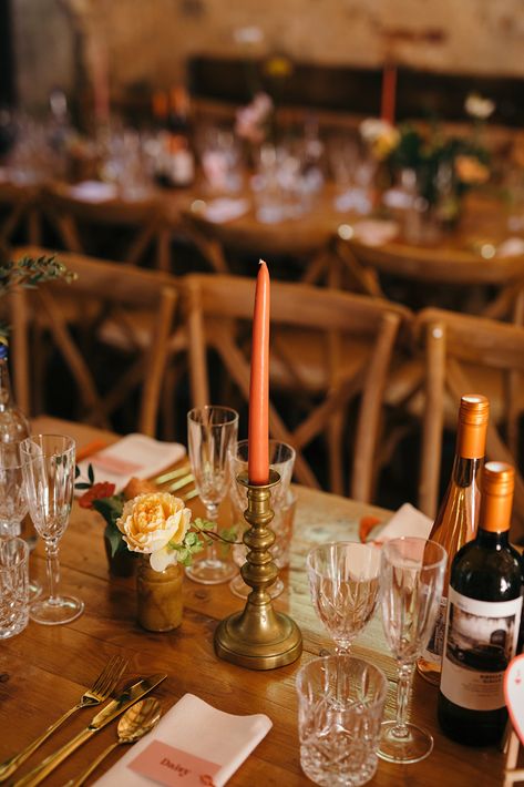 This shows a wedding dining set up. The focus is on the top of one of the tables, showing vases, glassware, brass candlestick with an orange candle, and napkins with personalised stationary. Brass Candlesticks Wedding, Candlestick Collection, Brass Candle Stick, Candle Sticks Wedding, Brass Candle Holder, Vintage Brass Candlesticks, Brass Candlestick, Brass Candle Holders, Brass Candle