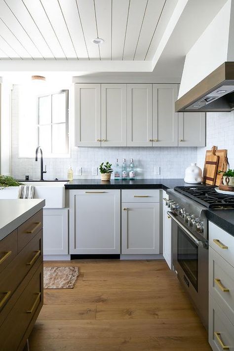 Light gray cabinets in a cottage kitchen feature black quartz countertops, white glazed backsplash tiles, and brass hardware. Grey Cabinets Black Countertop, Gray Cabinets Black Countertops, White Shaker Style Kitchen, Kitchen Black Counter, Light Grey Kitchen Cabinets, Greige Kitchen, Black Kitchen Countertops, Hardware Ideas, Light Grey Kitchens