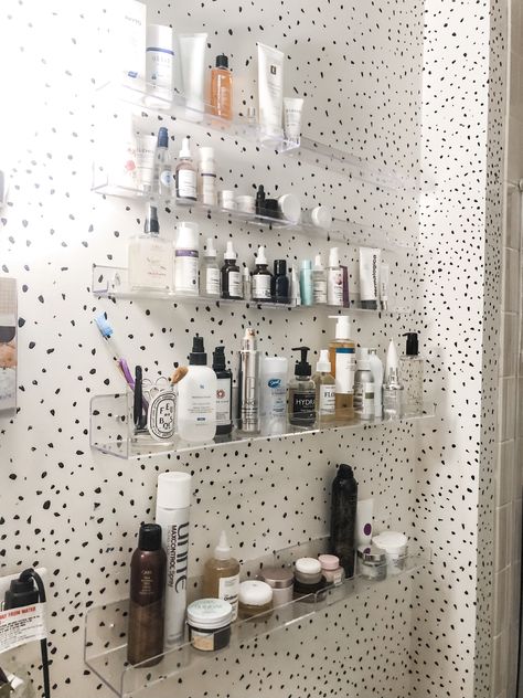 Bathroom with clear ledge shelves displaying and storing skincare products. Clear Acrylic Shelves Bathroom, Clear Floating Shelves Bathroom, Makeup Organization Wall Shelves, Acrylic Shelves In Bathroom, Bathroom Facial Organization, Skincare Shelves Bathroom, Acrylic Bathroom Storage, Bathroom Skincare Shelf, Skincare Wall Shelf