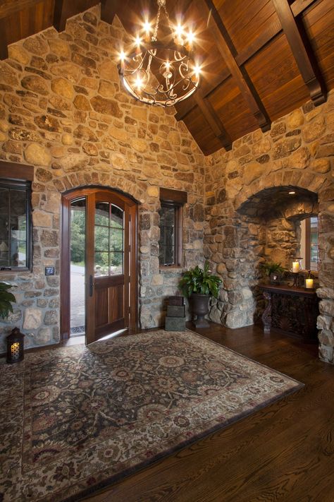 The foyer of this rustic mountain estate by Morgan-Keefe Builders makes a dramatic first impression with soaring timber ceilings, statement lighting, stone walls, and hardwood floors.  See more photos of this custom-built luxury mountain house at https://ecs.page.link/JYozd Stone Inside House, Lake House Entryway, Natural Stone Exterior House, Stone Foyer, Rustic Foyer Ideas Entryway, Luxury Mountain Homes Interiors, Mountain Homes Interiors, Mountain House Interior, Rustic Foyer