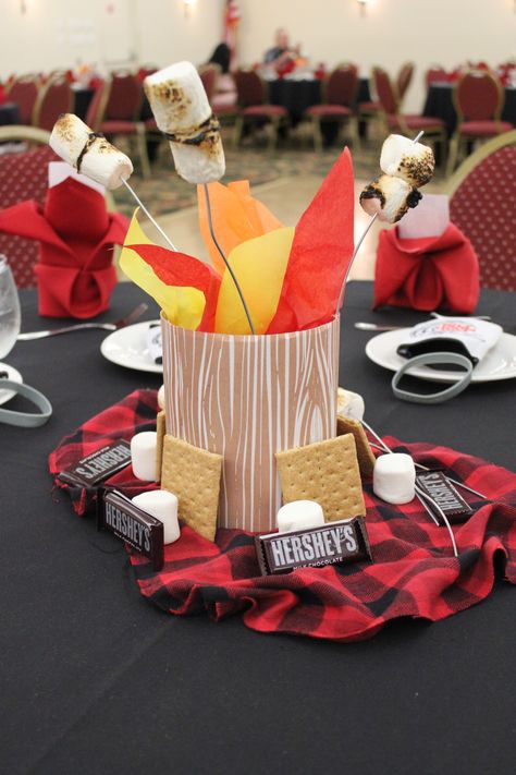 S’more and Camping Inspired Centerpieces -I used cardboard bird feeders (tops cut off) and Kleenex boxes from Michaels and wrapped with wood grain paper. Sand weighs down the box/gives placement to skewers. Dehydrate marshmallows prior. Put marshmallows onto skewer first and roast. Spray with matte finish spray paint which helps keep the ash from burning from falling off. Add some tissue paper for a fire affect and then place on top of sleeping bag like material with other S’mores-like goodies. Christmas Camping Theme, Camp Party Table Decor, Montana Themed Party, Camping Theme Table Decorations, One Happy Camper First Birthday Centerpiece, Camp Theme Centerpieces, Camping Retirement Party Ideas, Happy Trails Retirement Party, Campfire Centerpiece Ideas