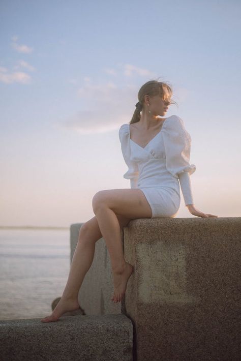 Woman in Dress Sitting on Rock against Blue Sky · Free Stock Photo Feminine Sitting Poses, Dress Poses Sitting, Sitting On Wall Pose, Elegant Sitting Pose, Woman Sitting Reference, Beach Model Photoshoot Poses, Lady Sitting Pose, Sitting On Ledge Pose, Figure Poses Reference Models