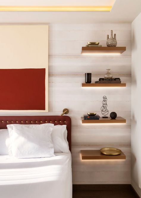 In this modern bedroom, four floating wood shelves with hidden lighting have been installed, with the lowest shelf at the correct height for a bedside table, while the other three shelves have been used to display decorative items. #BedroomDesign #BedsideTable #InteriorDesign #Shelving Bedside Wall Shelf Ideas, Floating Shelves As Bedside Tables, Bedside Shelving Ideas, Bedroom Nightstand Floating, Wall Shelf Bedside Table, Shelves As Bedside Tables, Shelf In Bedroom Wall, Bedroom Floating Shelves Night Stand, Floating Night Stand Ideas Bedrooms