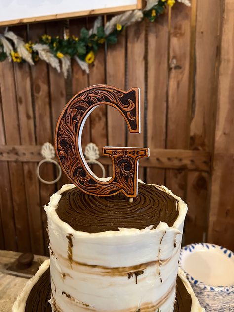 Add a touch of personalized charm to your special day with our Custom Ordered Leather Wedding Initial Cake Topper. Hand carved from quality leather, this topper features your initial on a 5-inch tall wooden letter. A unique and stylish addition to your wedding cake! Included are 2 wooden skewers that will slide into the bottom of the letter and easily slide down into your cake making it easy to insert and remove. This makes it super easy to display your new last name in your home after your spec Rustic Cake Toppers Wedding Country, Grooms Cake Outdoorsman, Western Wedding Isles, April Western Wedding, Leather Cake Topper, Mountain Western Wedding, Unity Branding Ceremony, Leather And Lace Wedding Theme, Western Wedding Cake Toppers