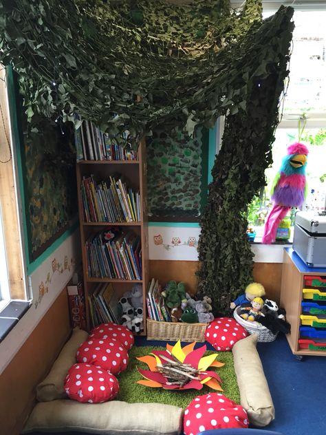 Woodland reading area  We used the bookshelf as the trunk and hung cargo netting to create the leaves.  We bought a cheap £5 BBQ and used the base for the campfire, I stuck flames shapes to the bottom and added twigs. We bought hessian fabric and created logs and toadstools. Got the rug from Amazon for £10! Children love it! Ambient Lighting Classroom, Woodland Book Corner, Woodland Reading Nook, Woodland Reading Corner, Forest Reading Corner, Fantasy Classroom Decor, Book Area Ideas, Mushroom Classroom, Enchanted Forest Classroom