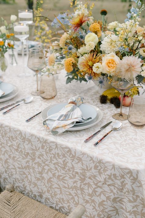 A wildflower floral arrangement and colorful wine glasses atop a neutral patterned linen with wicker chairs and a colorful napkin. Stradley Davidson's Ascot Garden was used for the napkin and Fitz Almond for the table linen. Pattern Table Cloth Wedding, Colorful Wedding Linens, Patterned Wedding Table Linens, Patterned Tablecloth Wedding, Wedding Linens Ideas, Floral Tablecloth Wedding, Linen Tablecloth Wedding, Wedding Drinkware, Reception Table Settings