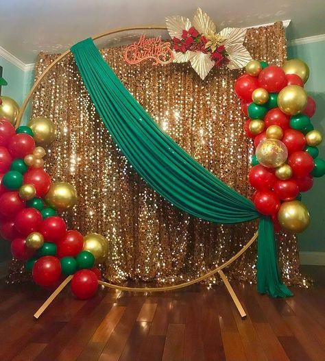 Set up a sparkling backdrop for your Christmas party using attractive decor elements. Cover the backdrop stand with shimmery gold sequin curtains for an enticing allure. Place a gold round arch at the front and arrange red, gold, and green balloons on it to impart a peppy appeal to your party decor. Also, stylishly drape green fabric and arrange red flowers along with gold leaves on the stand oozing oodles of glimmer and shimmer. Backdrop With Curtains, Flowers And Balloons, Green Christmas Decorations, Sequin Curtains, Christmas Party Backdrop, Christmas Arch, Christmas Balloon Decorations, Birthday Decorations At Home, Deco Ballon