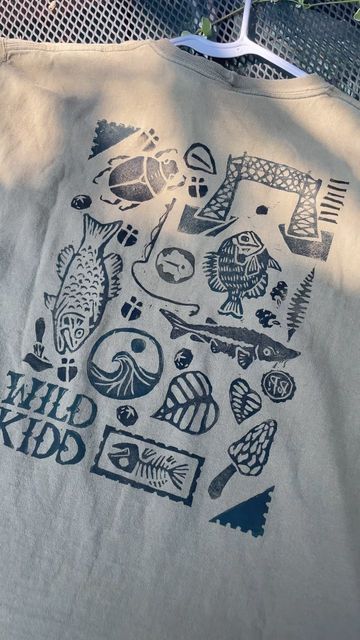 Wild Kidd Design | Anna Kidd on Instagram: "Which stamp is your favorite? 🐟  Got the block prints unpacked and had to whip a couple pieces together for the market tomorrow (cross your fingers for no rain :)  Block print collages are a personal favorite and I love the endless combinations that can come out of it while keeping cost lower than a hand sewn piece AND turning trash into treasure  Truly a win win win for me, you and mama earth 🌍 ❤️  Any stamp recommendations?  #trashtotreasure #upcycling #upcycledfashion #blockprinting #natureartist #minnesotaartist #wearableart" Block Printing Clothes, Block Print T Shirt, Block Print Shirt, Trash Into Treasure, Mama Earth, Cross Your Fingers, Earth Mama, Nature Artists, Merch Ideas