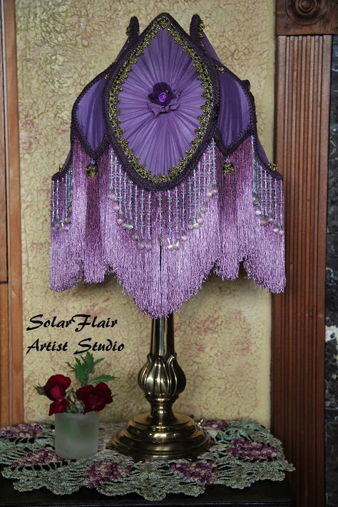 Purple Victorian style tulip lamp shade. Two shades of purple with fringe and beads, handmade tassels, french trim, silk rosettes and metallic trim. Hand dyed, handmade by Georgette Conrad. Lamp shade is on a brass tulip lamp. Purple Victorian Lampshade, Victorian Lamp Shades Diy, Antique Lamps Victorian, Purple Lamp Shade, Victorian Lamp Shades, Victorian Lamp Shade, Victorian Lamp, Purple Lamp, Vintage Lampshades