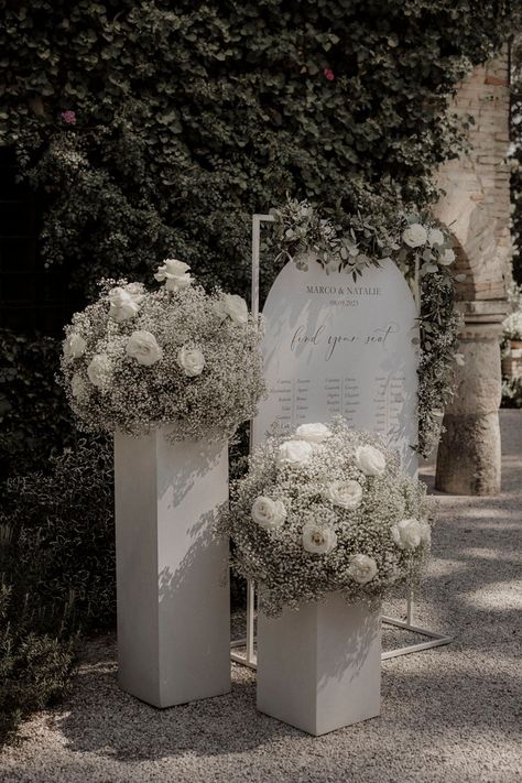 White roses and white gypsophila with white wedding table plan signage White Rose Wedding Arrangements, White Flower Table Arrangements Wedding, Wedding Decorations White Roses, White Flowers Decoration Wedding, White Flower Wedding Backdrop, Wedding Table Decorations White Flowers, White Rose Isle Wedding, Diy White Flower Arrangements, Head Table Wedding Decorations Backdrops