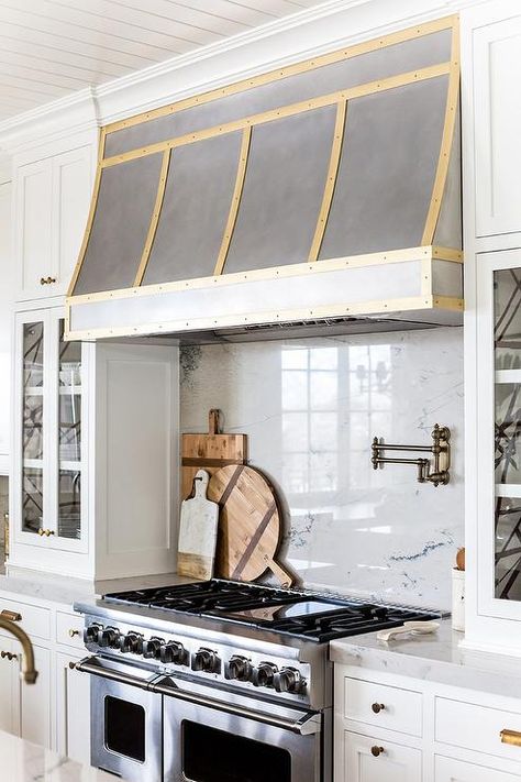 Exquisite kitchen features a steel kitchen hood accented with brass trim which stands over a marble cooktop backsplash lined with a swing arm pot filler and a stainless steel stove with dual ovens flanked by glass door cabinets with backs of shelves lined with black and white abstract wallpaper, Kelly Wearstler Channels Wallpaper. Kitchen Hood Ideas, White Kitchen Traditional, Kitchen Vent Hood, Oven Hood, Kitchen Vent, Kitchen Range Hood, Kitchen Hoods, Gold Kitchen, Kitchen Stove