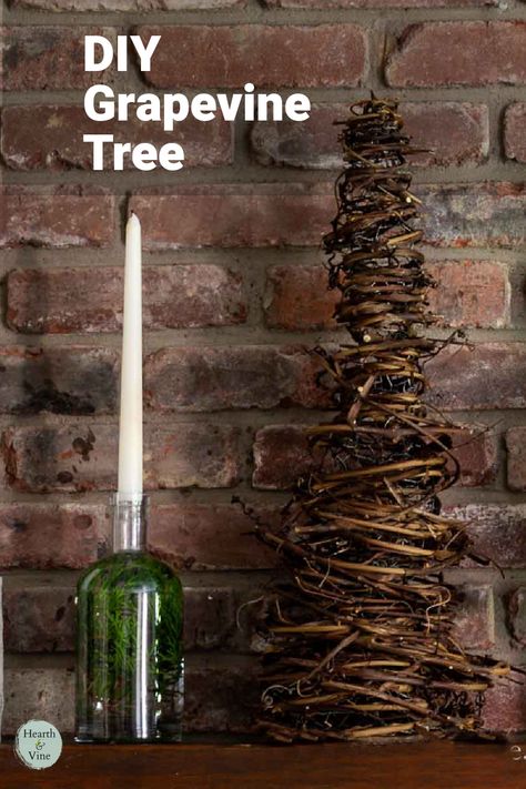 A cone shaped tree made from grapevines sits on a mantle with a bottle and candle. Things To Make With Grape Vines, Grapevine Garland Christmas Tree, Grapevine Trees Diy How To Make, Grapevine Craft Ideas, Diy Grapevine Garland, Crafts With Grape Vines, Grapevine Garland Front Door Christmas, Diy Grapevine Tree, Grapevine Crafts Diy