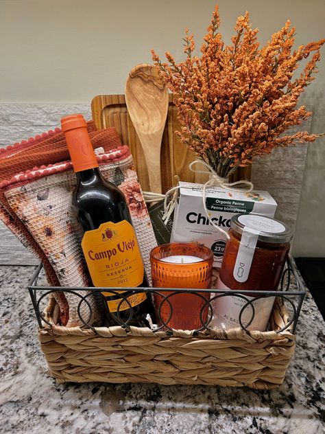 Fall themed gift basket with orange and wood accents. Gift basket is pasta date-night themed and includes red Italian wine, gluten free chickpea pasta, pasta sauce, candle, kitchen towel, wooden spoon and orange accents. Accents are decorative floral and tweed. Pasta Night Gift Basket, Natal, Wine And Pasta Gift Basket Ideas, Dinner In A Basket Gift, Charcuterie Themed Gift Basket, Meal Gift Basket Dinners, House Warming Basket Diy, Charcuterie Basket Ideas, Fall Gift Baskets Ideas