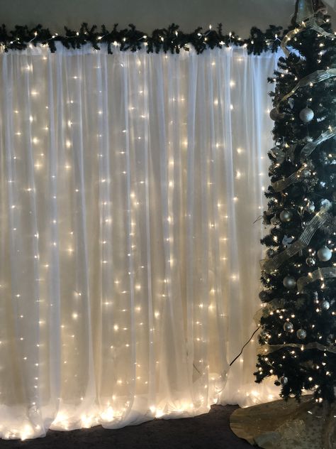 Christmas Backdrop (Pipe and Drape with string lights and greenery. Christmas Drapes Ideas, Winter Theme Backdrop, Christmas Pictures Backdrop, Winter Party Backdrop, Diy Santa Photo Backdrop, Simple Christmas Backdrops For Photos, Christmas Wedding Photo Backdrop, Simple Christmas Photo Backdrop, Diy Photo Backdrop Christmas