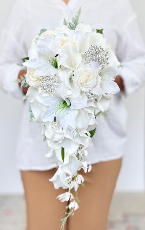 "This beautiful white cascading bouquet is one our our luxurious, high quality bouquets. It is made out real to touch roses, real touch calla lilies, real touch lilies, a spray of silk orchids, silk hydrangeas and a touch of dusty miller. The floral used in this bouquet   feel just like real flowers. This bouquet can also can be arranged with or without shimmering rhinestone brooches. Perfect for your white, minimalistic, or modern wedding!   Dimensions: Measures 10\" across and cascades 23\" long WITH the brooches and 9\" x 23\" WITHOUT the brooches. If you are interested in a bouquet that is a different size or shape for your bridesmaids, please send me a message so that I can accommodate your request.   VISIT MY SHOP  https://www.etsy.com/ca/shop/AdoredOccasions?ref=hdr_shop_menu Check Bride Boutique Flowers, Bridesmaid Floral Bouquet, Wedding Bouquets Real Flowers, Wedding Bouquet Calla Lily, Bride White Bouquet, Long Wedding Bouquets Brides, Hanging Wedding Bouquets, Teardrop Wedding Bouquet, Orchid And Hydrangea Bouquet