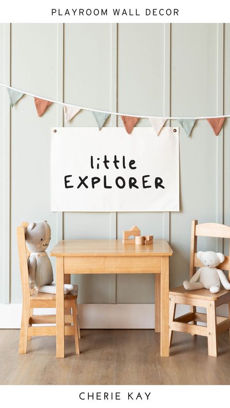 Little Explorer canvas wall decor hanging above a wooden kids table and chairs in a playroom or nursery setting. The room features soft green panel walls, neutral-colored bunting, and plush toys, creating a cozy and inviting space for children. This modern, gender-neutral wall art is perfect for adding a playful and adventurous touch to kids' room decor. Playroom Wall Color Ideas, Adventure Theme Boys Room, Where The Wild Ones Play, Cool Kids Club, Kids Room Sign, Classroom Wall Decor, Playroom Wall Decor, Baby Shower Inspiration, Kids Room Wall Decor