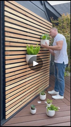 How to make a slatted planter wall | This is such an easy DIY and perfect for spring! We love these ceramic pots we found at Walmart! Incredible quality and come in different sizes! 🔗 Below... | By Emyludesigns | You wanted to know how we made this DIY slatted planter wall? Well let me show you. First I started with five and a half inch cedar fence pickets. To turn them into slats I ripped each fence picket into thirds. It's about one and six eighths of an inch. Then I trimmed the bevel off and made sure all the pieces were the same length and then sanded one side down smooth to remove that rough sun look. Then I made a frame using two by twos and two by fours. Since we wanted our frame to cover the backside of our chimney. It needed to be 70 inches by 70 inches. I assembled the frame tog Side Return Garden Ideas, Slatted Planter, Side Return Garden, Diy Stone Walkway, Diy Planters Pots, Wall Planters Outdoor, Diy Wall Planter, Cedar Fence Pickets, Fence Picket