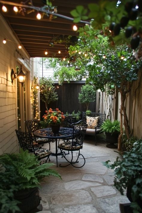 Cozy outdoor patio with string lights, wrought iron table and chairs, surrounded by lush greenery. Small Yard Seating Area, Alternative Patio Ideas, Covered Patio Garden Ideas, Cement Patio Designs, Southern Patio Ideas, Cozy Backyard Ideas Landscaping, Small Patio Oasis, Back Patio Ideas Covered, Tiny Outdoor Patio Ideas