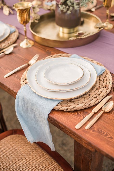 Rustic place setting with light blue linen napkin, gold flatware, & rattan placemat Farmhouse Dining Table Place Settings, Rustic Table Setting Home, Rattan Table Setting, Rattan Placemats Table Settings, Gold Flatware Table Setting, Rattan Chargers Table Setting, Napkin Placement Ideas, Dining Room Place Settings, Rustic Place Setting