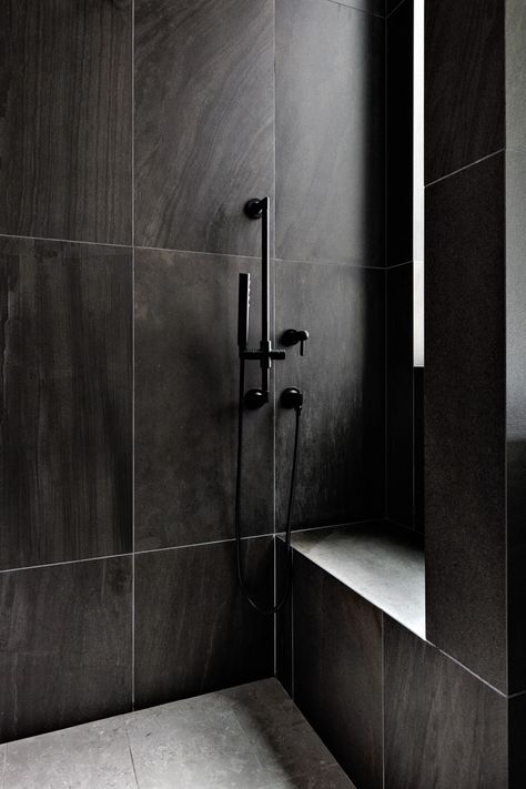 The couple’s bathroom shower is a moody alcove covered with deep black Emilceramica porcelain tile. Dark Brizo shower fixtures enhance the drama. Noir Veined Tile Bathroom, Black Large Tile Bathroom, Dark Tile Shower Ideas Small Bathrooms, Black Walk In Shower Ideas Tile, Shower Tile Ideas Black, Dark Tile Bathroom Ideas, Dark Tiles In Bathroom, Dark Bathroom Tile Ideas, Dark Gray Bathroom Tile