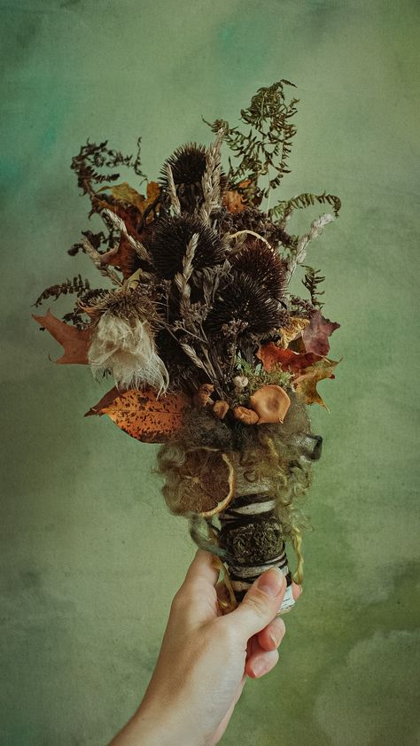 A hand holds up a dried floral bouquet of flowers, autumn leaves, lemon slices, mushrooms, and wool in a birch bark holder Witch Bouquet Wedding, Forest Themed Bouquet, Fantasy Flower Bouquet, Leaf Bouquet, Bone Bouquet, Witchy Flower Bouquet, Mushroom Bouquet, Dark Forest Bouquet, Mushroom Wedding Decor