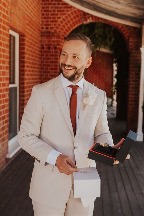 A groom smiling to someone off camera holding a gifted watch. Cocktail Attire Men Wedding, Cream Suits For Men, Garden Party Outfits, Cocktail Attire Men, Groom And Groomsmen Suits, Cream Suit, Modern Groom, Orange Suit, Burnt Orange Weddings