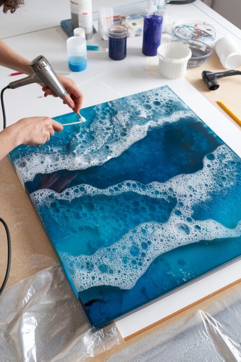 Artist using a heat gun to create a resin ocean wave art on a square canvas. Epoxy Resin Art Painting, Blue Resin Art, Art With Resin, Resin Techniques, Beach Resin, Acrylic Pouring Techniques, Ocean Resin, Art Skills, Sand Textures