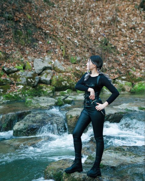 A girl in black leather outfit standing in the middle of the forest on the rock on a small stream reaching for a dagger Violet Sorrengail Costume, Fourth Wing Cosplay, Violet Sorrengail Cosplay, Dragon Rider Outfit, Wing Cosplay, 4th Wing, Empyrean Series, Violet Sorrengail, Warrior Outfit