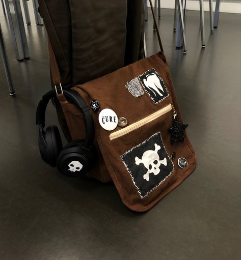 A brown bag with lots of black and white selfmade accessories Cross Body Bags Aesthetic, Punk Messenger Bag, Bag Patches Aesthetic, Goth Backpack Diy, Goth Bag Diy, Punk Bag Diy, Headphone Customization, Bag Pins Ideas, Cross Body Bag Aesthetic