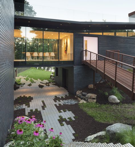 This sculptural home set deeply into the hillside of the Stillwater countryside features charred wood siding (shou sugi ban), cantilevered roof overhangs, and a glass bridge that visually separates the public and private spaces of the house. House Bridge Walkways, Bridge Entrance To House, Glass Atrium House, Bridge To House Entrance, Houses With Bridges, House With Bridge, Bridge Homes, Cantilever Roof, Greenhouse Attached To House