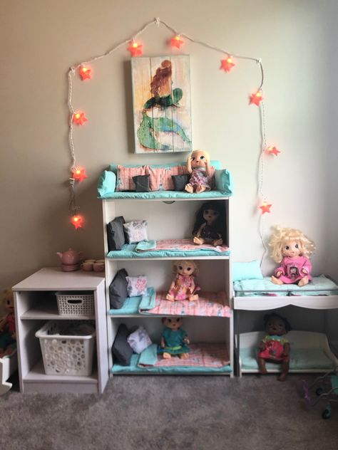 Wanted to create a baby doll nursery for my daughter that was easily organized and appealing to the eye in our playroom. (Yes I’m a mom that likes to have a organized & clean playroom) So I bought a bookshelf at Target and used foam, fabric and hot glue to make the bedding and top sitting area. I think it turned out really cute and my daughter loves it, the best part was the cost that ended up being much less than if I were to have purchased ready made beds and a doll couch. 😊 Playroom Organization Dolls, Reborn Doll Storage Ideas, Doll Storage Playroom, Doll Storage Ideas Organizing Bedroom, Baby Doll Beds, Doll And Accessory Storage, Babydoll Nursery Playroom, Doll Playroom Setup, Babydoll Playroom