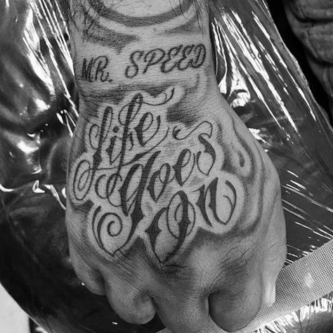 Shaded Script Hand Life Goes On Tattoos For Males Life Goes On Hand Tattoo, Life Goes On Tattoo Design, Life Goes On Tattoos, Giver Tattoo Ideas, Such Is Life Tattoo, Giver Tattoo, Hand Tattoos For Guys Words, Life Goes On Tattoo Ideas, Life Is Good Tattoo