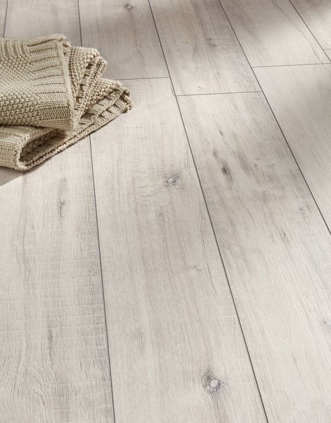 Gala Oak White takes inspiration from natural oak and reproduces its organic charm accurately with rustic grain patterns, a textured surface and 4-sided V-groove planks. A convenient and more affordable alternative to solid wood flooring, this laminate floor is designed to handle the pressures of heavy foot traffic anywhere, from family homes to busy commercial spaces. The 12mm thick planks measure 188mm in width, making them perfect for medium-sized and larger rooms. Easy to clean and to mainta White Wood Laminate Flooring, White Laminate Flooring, White Wooden Floor, Beach House Flooring, Direct Wood Flooring, White Wood Floors, Residential Flooring, Oak Laminate Flooring, Lvp Flooring