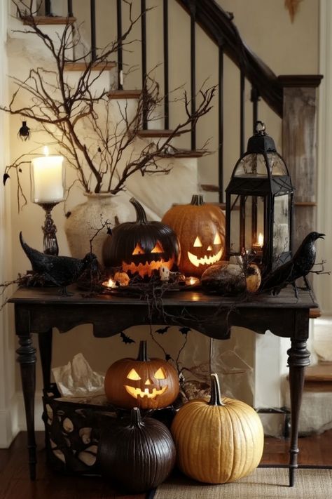 Halloween-themed table with carved pumpkins, candle lanterns, and spooky decorations by a staircase. Entry Halloween Decor, Halloween Decor Inside House, Vintage Halloween Home Decor, Halloween Inside Decor, Disco Halloween Decor, Inside Halloween Decor, Diy Indoor Halloween Decorations, Table Halloween Decor, Victorian Halloween Decorations